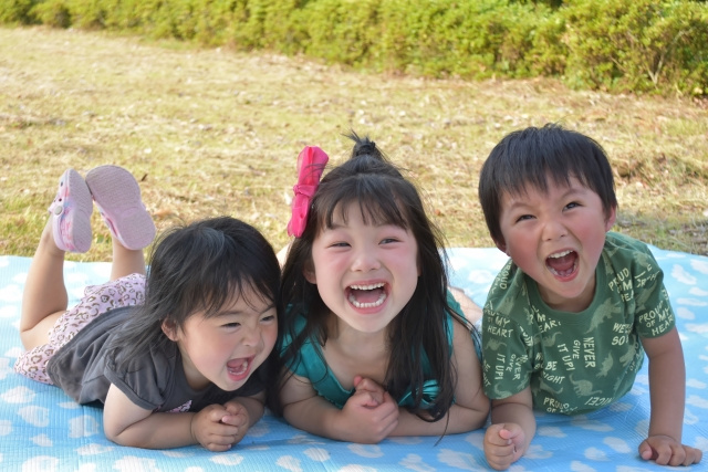 レジャーシートの上に寝転んで笑っている三人の子供