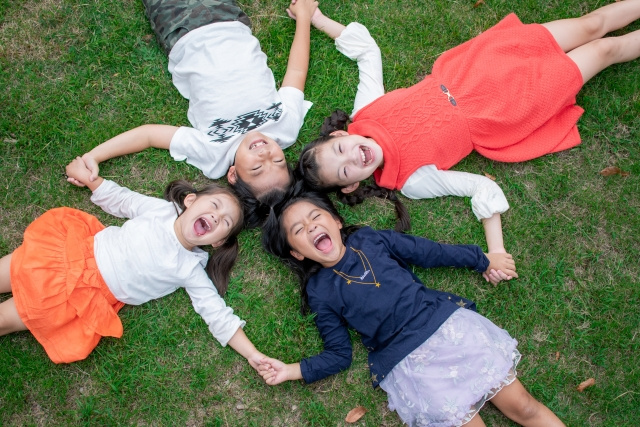 手を繋いで芝生であおむけになっている4人の子ども