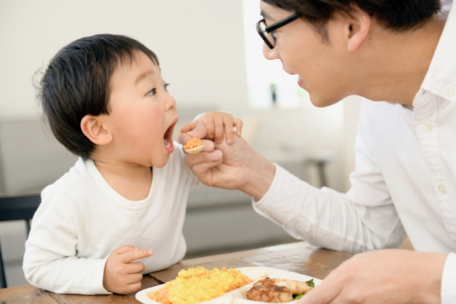息子の口に食事を運ぶ父と、口を開けてそれを食べようとしている幼児