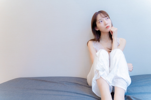 ベッドに座って考え事をしている女性